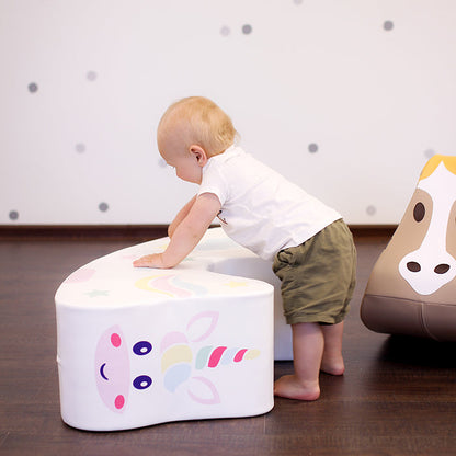 A baby standing next to a unicorn foam rocking toy