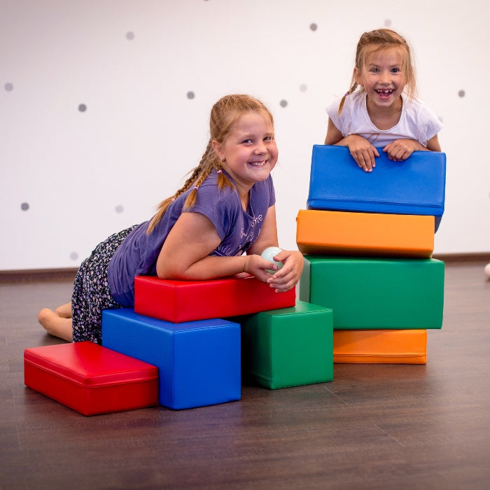 Two girls having imaginative adventures with IGLU Soft Play's Soft Foam Building Blocks - Mini Builder in a room.