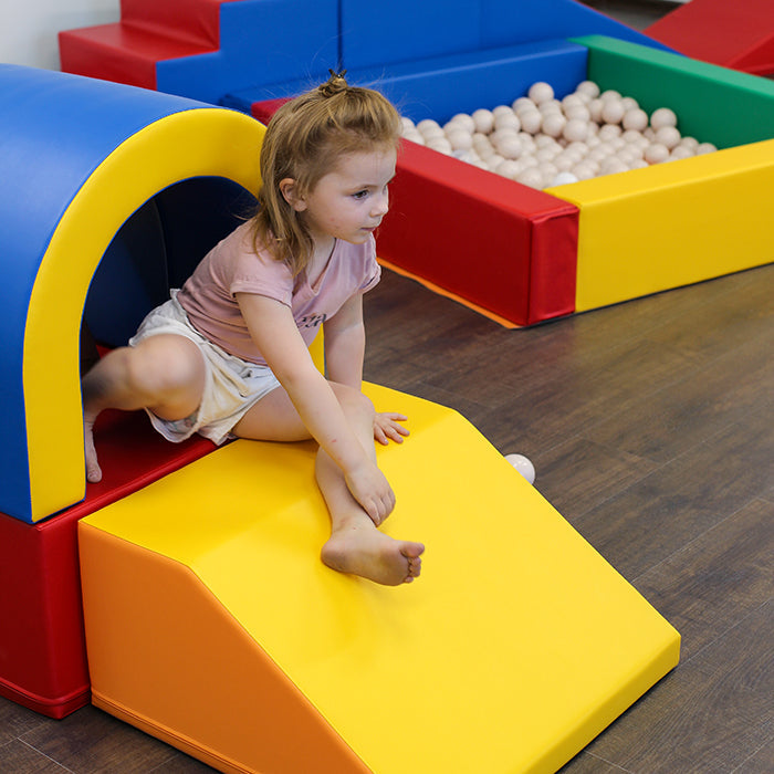 A girl playing on a bright yellow soft play foam slide