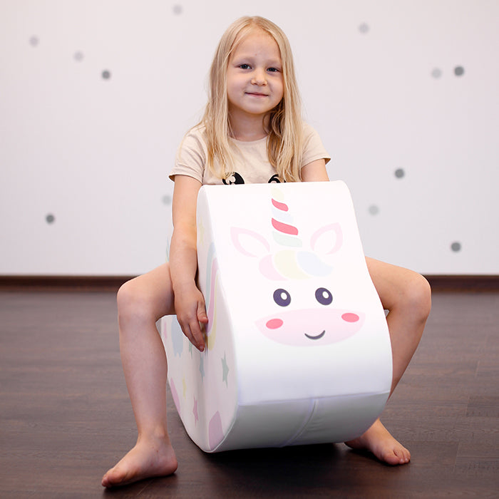 A girl sitting on a unicorn foam rocking toy 